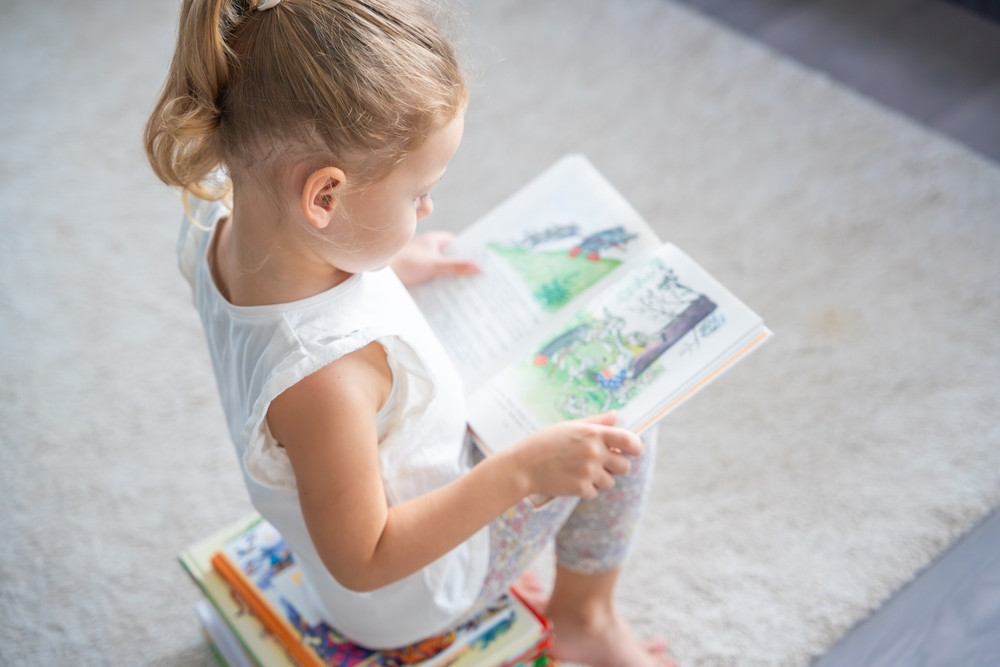 Little,Girl,Is,Sitting,On,Stack,Of,Children's,Books,And