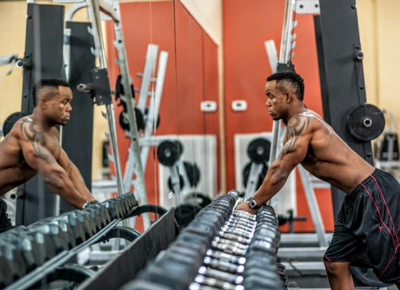 Muscular man exercising with dumbbells in gym, emphasizing strength and fitness.