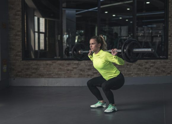 Dedicated woman in neon activewear performs a weighted squat in an indoor gym setting.